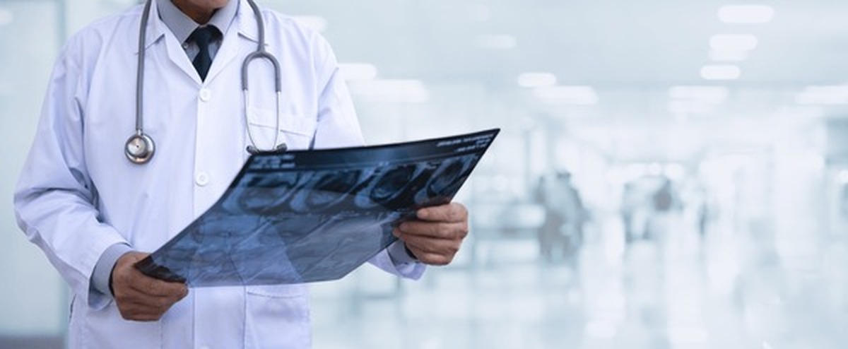 Clinician in a white coat examining an imaging film in a hospital corridor